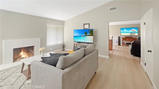 living area with high vaulted ceiling, visible vents, a fireplace, baseboards, and light wood-style floors