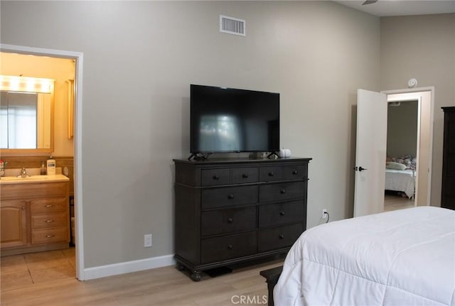 bedroom with a sink, light wood-type flooring, visible vents, connected bathroom, and baseboards