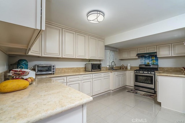 kitchen with stainless steel appliances, a toaster, a sink, under cabinet range hood, and light tile patterned floors