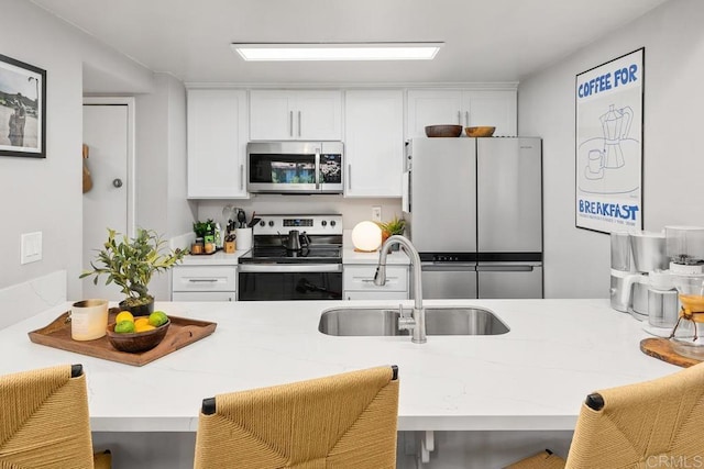 kitchen featuring a sink, a kitchen breakfast bar, white cabinetry, appliances with stainless steel finishes, and light stone counters
