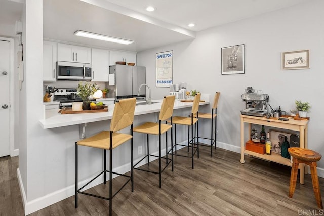 kitchen with a peninsula, dark wood finished floors, a breakfast bar area, and appliances with stainless steel finishes