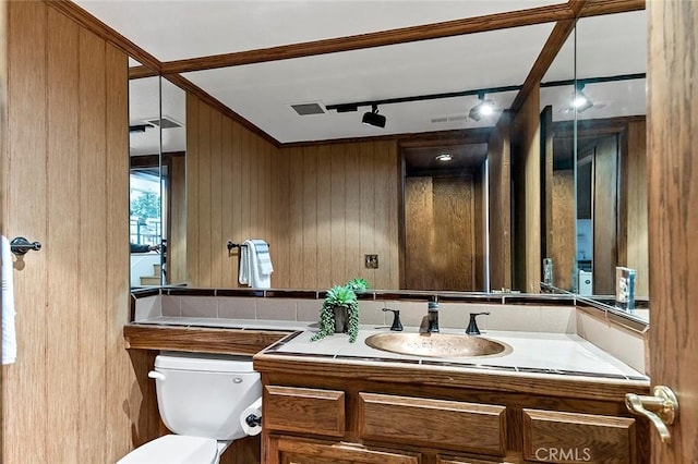 half bath with ornamental molding, toilet, vanity, and wood walls