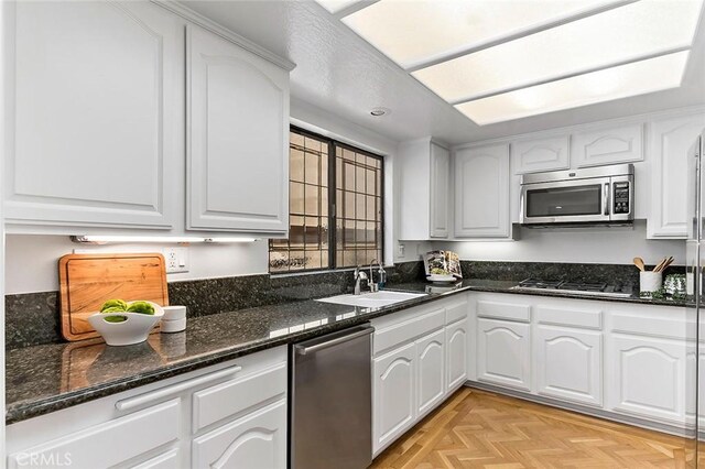 kitchen featuring white cabinets, stainless steel appliances, a sink, and dark stone counters