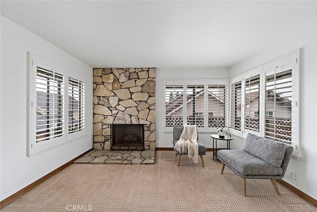 living area featuring a stone fireplace, baseboards, and carpet