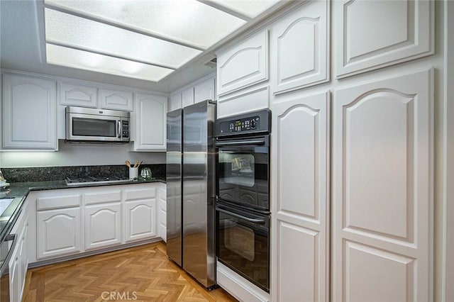 kitchen with white cabinetry, stainless steel appliances, and dark stone countertops