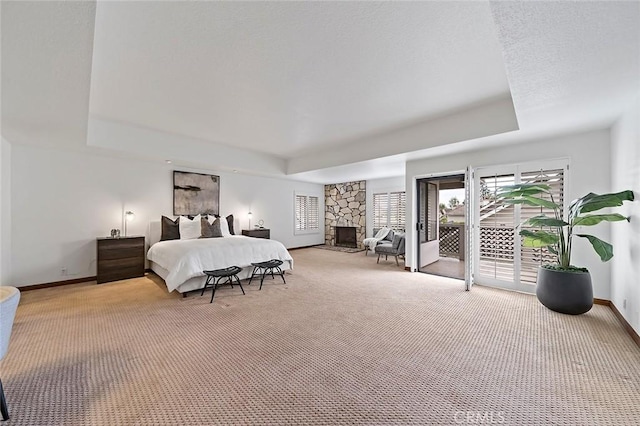 bedroom with a tray ceiling, access to exterior, baseboards, a fireplace, and light colored carpet