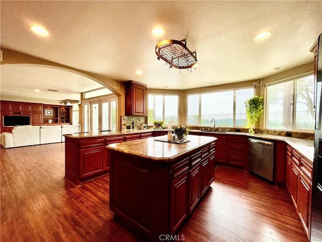 kitchen featuring dark brown cabinets, stainless steel dishwasher, arched walkways, a kitchen island, and dark wood-style flooring