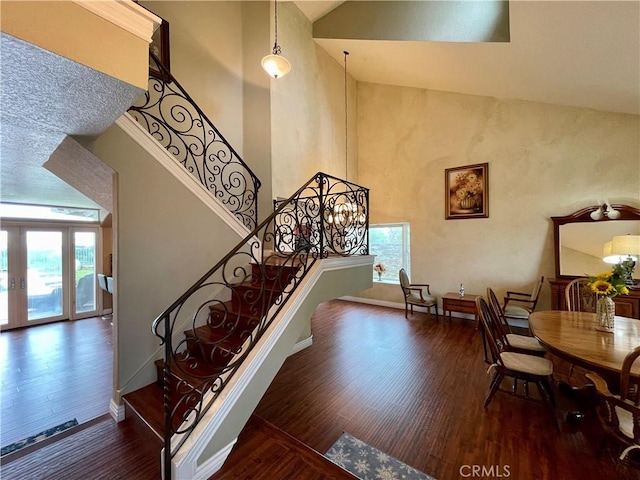 staircase featuring plenty of natural light, baseboards, wood finished floors, and high vaulted ceiling