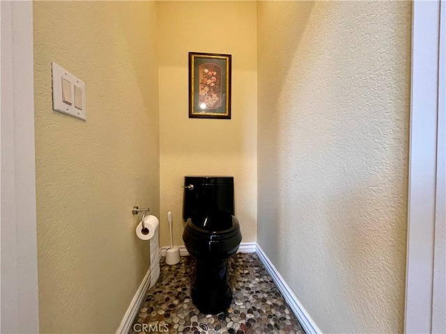 bathroom with a textured wall, baseboards, and toilet