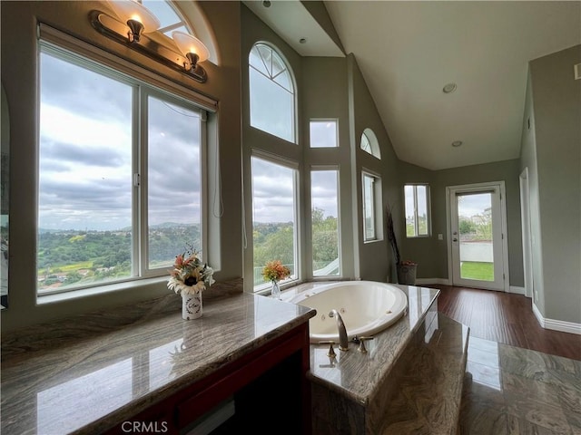 bathroom featuring high vaulted ceiling, baseboards, a tub with jets, and wood finished floors