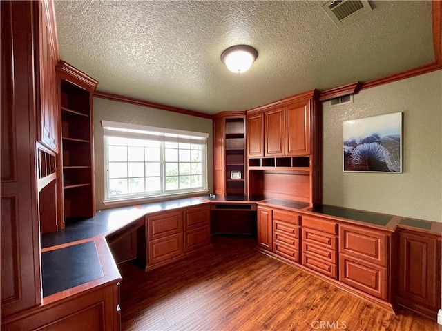 unfurnished office featuring crown molding, wood finished floors, a textured ceiling, built in study area, and visible vents