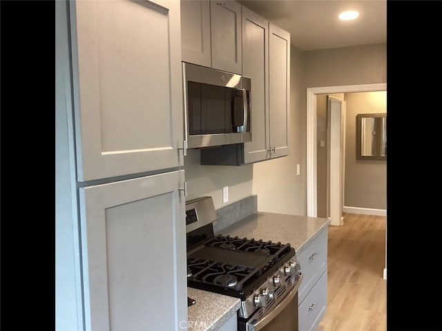 kitchen with light wood-type flooring, stainless steel appliances, and light stone counters