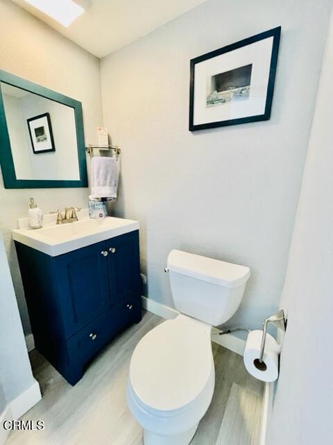 half bathroom featuring baseboards, wood finished floors, vanity, and toilet