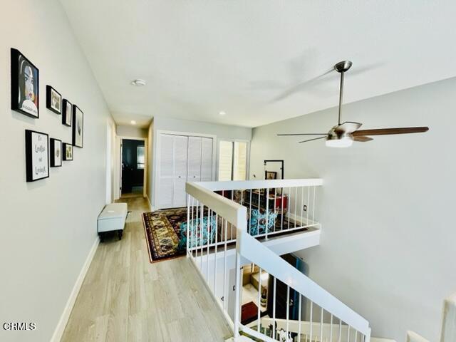corridor with recessed lighting, wood finished floors, baseboards, and an upstairs landing