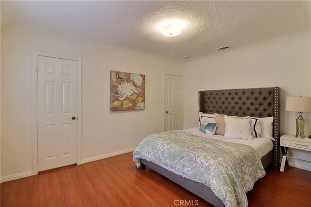 bedroom with baseboards, wood finished floors, visible vents, and a textured ceiling