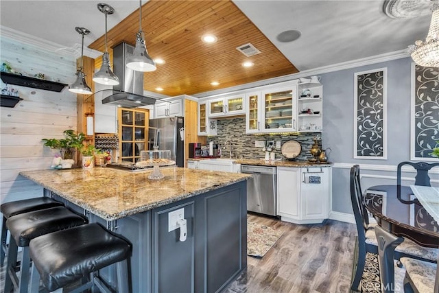 kitchen with visible vents, island range hood, a peninsula, appliances with stainless steel finishes, and a breakfast bar area