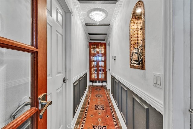corridor featuring crown molding, a wainscoted wall, and a decorative wall