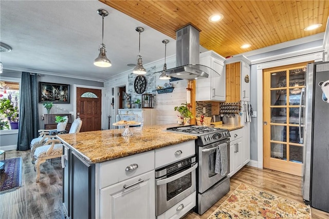 kitchen with a peninsula, island exhaust hood, white cabinetry, appliances with stainless steel finishes, and ornamental molding