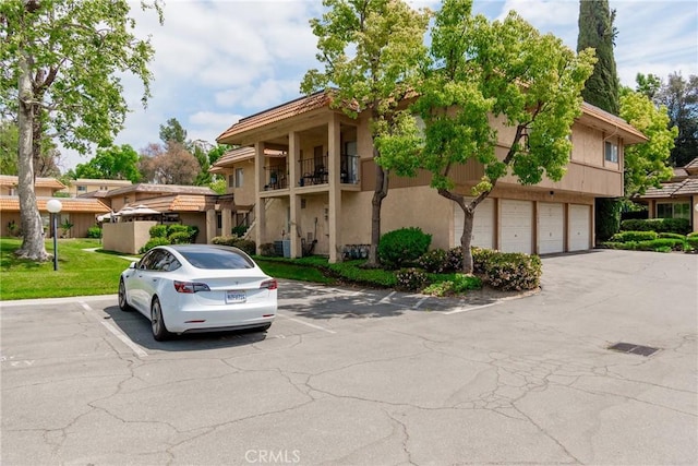 view of front of property with stucco siding, uncovered parking, a front lawn, and a balcony