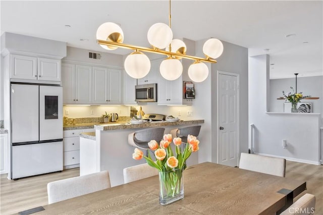 372 W Linden Dr, Orange, CA 92865 - kitchen featuring fridge, stainless steel microwave, light wood finished floors, white cabinetry, and hanging light fixtures