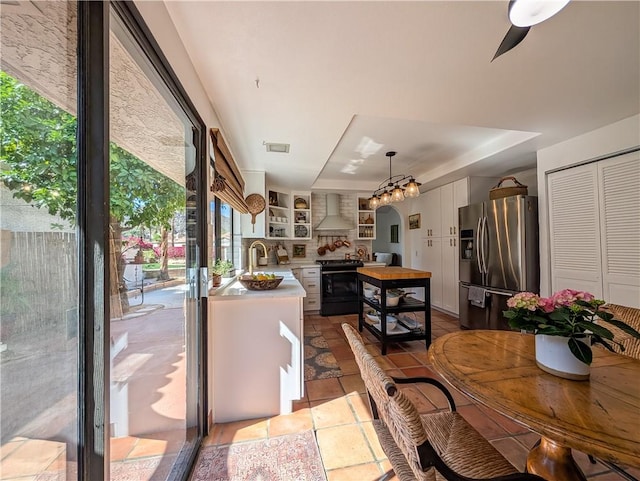 48143 Calle Seranas Ln, Quinta, CA 92253 - kitchen with black range with electric cooktop, stainless steel fridge with ice dispenser, a healthy amount of sunlight, and wall chimney exhaust hood