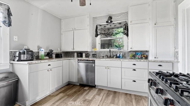 kitchen featuring white cabinets, stainless steel appliances, backsplash, a sink, and light wood-style flooring