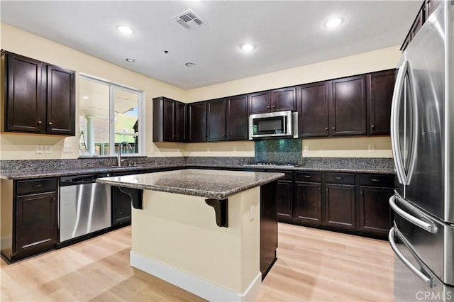 kitchen with dark stone countertops, a sink, light wood-type flooring, appliances with stainless steel finishes, and visible vents
