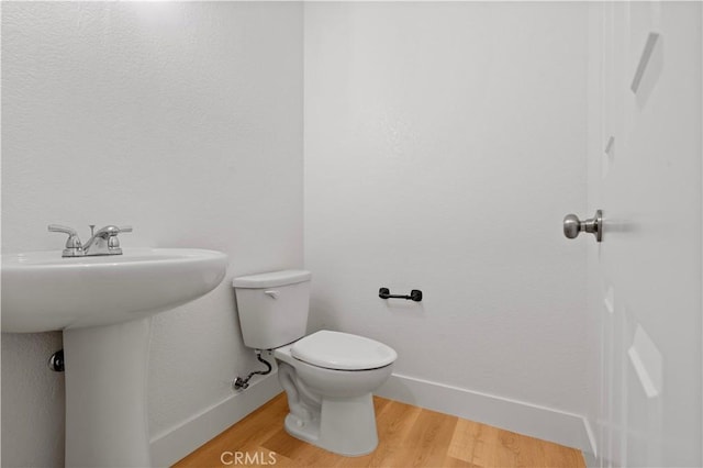 bathroom featuring wood finished floors, toilet, baseboards, and a sink