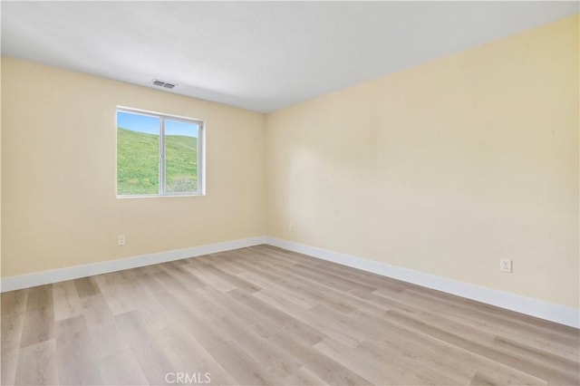 unfurnished room featuring visible vents, light wood finished floors, and baseboards