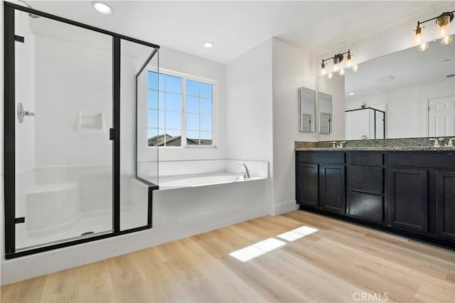 bathroom with wood finished floors, double vanity, a sink, a bath, and a stall shower