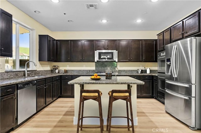 kitchen featuring dark stone countertops, a sink, light wood-style flooring, appliances with stainless steel finishes, and a breakfast bar area