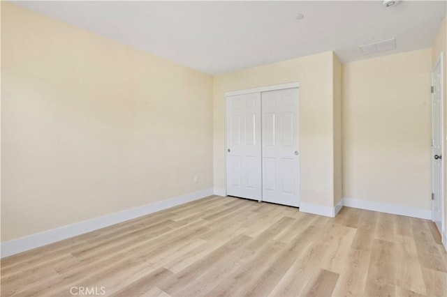 unfurnished bedroom featuring light wood finished floors, baseboards, and a closet