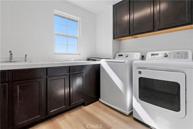 laundry room featuring cabinet space, a sink, light wood-type flooring, and independent washer and dryer