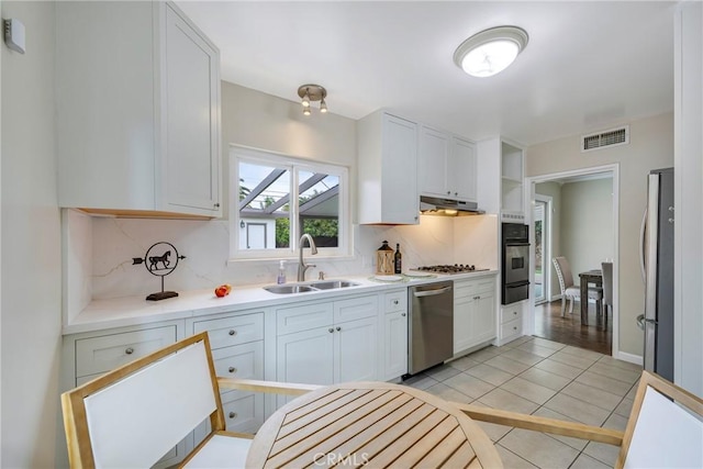 kitchen featuring stainless steel appliances, a sink, tasteful backsplash, visible vents, and under cabinet range hood