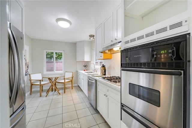 kitchen with stainless steel appliances, a sink, white cabinetry, light countertops, and under cabinet range hood