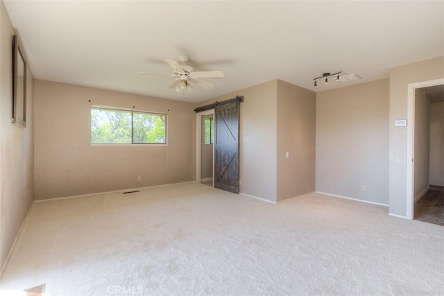 unfurnished bedroom with a barn door, light carpet, ceiling fan, and baseboards