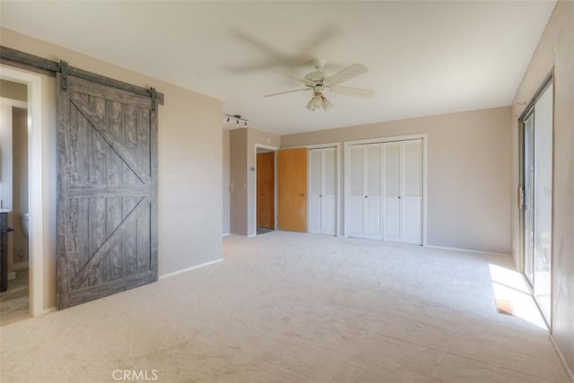 unfurnished bedroom with a barn door, two closets, baseboards, and carpet