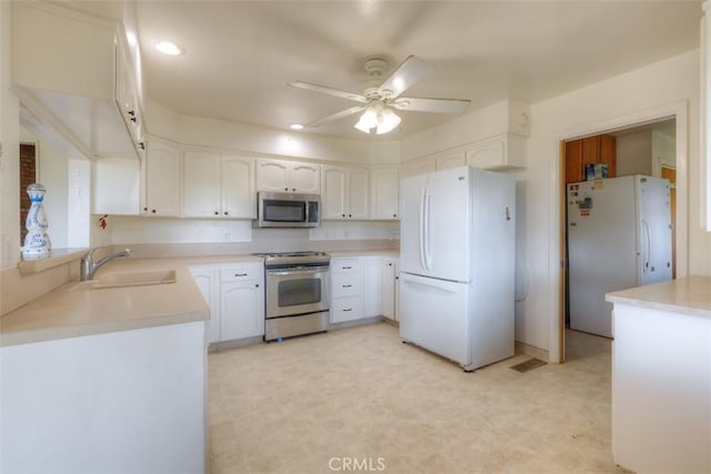 kitchen featuring a ceiling fan, a sink, light floors, stainless steel appliances, and white cabinetry