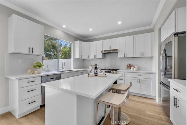 kitchen featuring under cabinet range hood, stainless steel appliances, a sink, a kitchen island, and a breakfast bar area