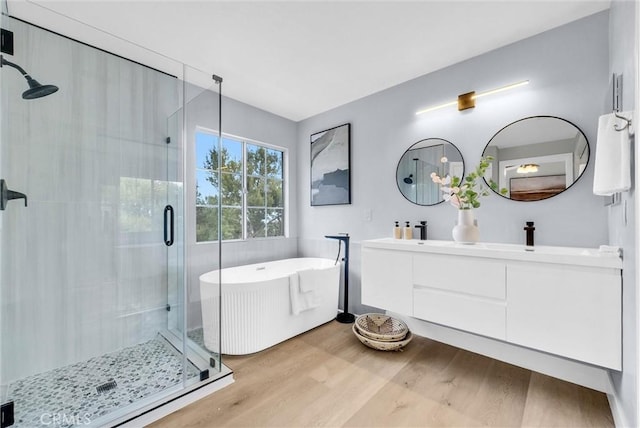 full bath featuring a sink, double vanity, a freestanding bath, wood finished floors, and a shower stall