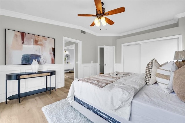 bedroom featuring light wood finished floors, a wainscoted wall, visible vents, a closet, and crown molding