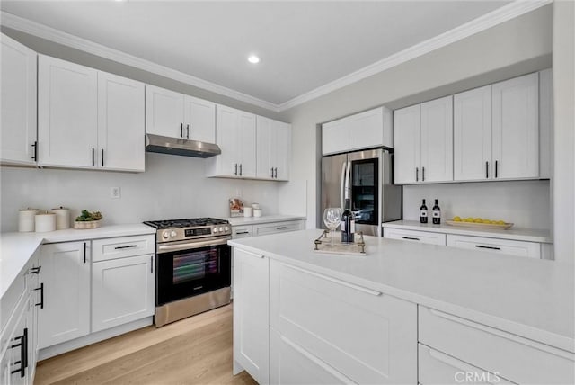 kitchen with white cabinets, under cabinet range hood, appliances with stainless steel finishes, and crown molding