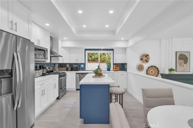 kitchen featuring tasteful backsplash, a tray ceiling, a kitchen bar, wall chimney exhaust hood, and appliances with stainless steel finishes