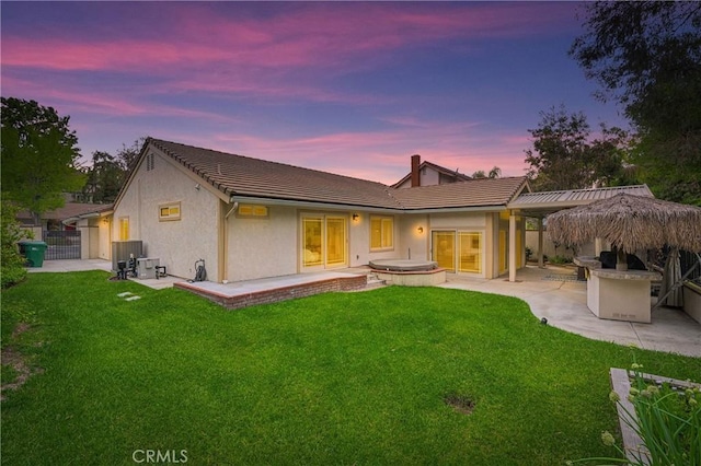 back of house at dusk featuring a lawn, fence, a patio, and stucco siding