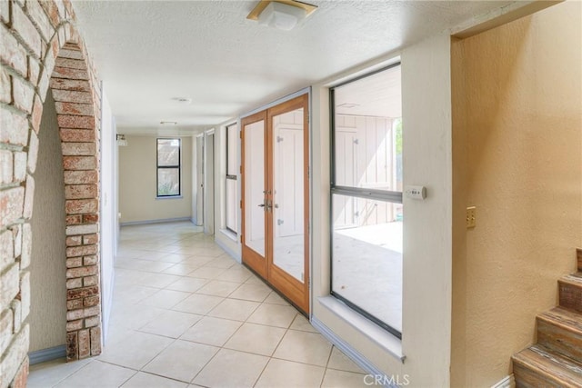 corridor with a textured wall, a healthy amount of sunlight, a textured ceiling, and light tile patterned floors