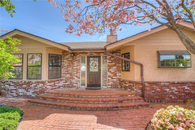 entrance to property with a chimney, brick siding, and stucco siding