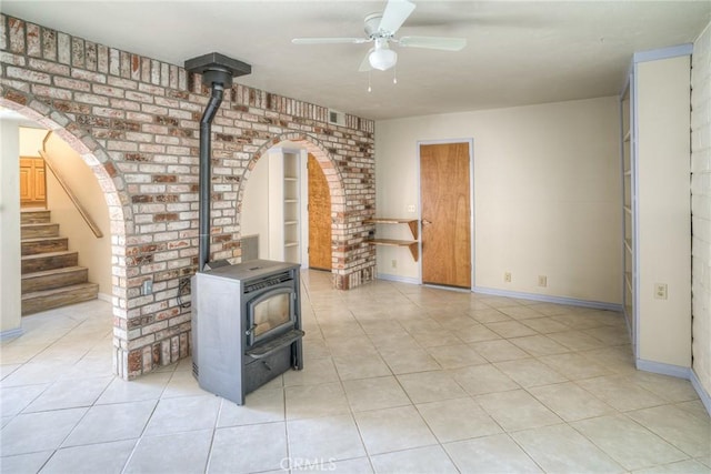 unfurnished living room with a wood stove, a ceiling fan, baseboards, and light tile patterned floors