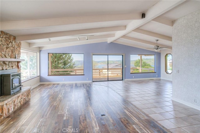 unfurnished living room with vaulted ceiling with beams, baseboards, a wood stove, and a ceiling fan