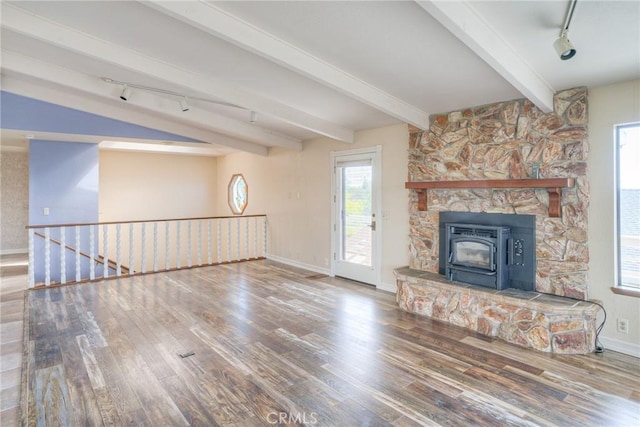 unfurnished living room with track lighting, baseboards, a wood stove, and wood finished floors