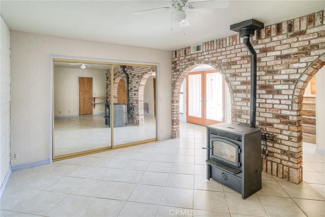 unfurnished living room with tile patterned flooring, a wood stove, a ceiling fan, arched walkways, and brick wall